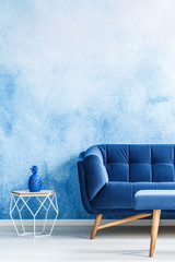 Copy space monochromatic living room interior with plush, navy blue couch and metal side table...