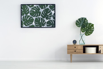 Leaves poster on white wall in living room interior with wooden cupboard. Real photo