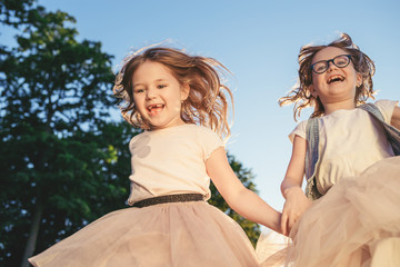 Fototapeta na wymiar Two joyful girls running, jumping and smiling. Summer activity and leisure.