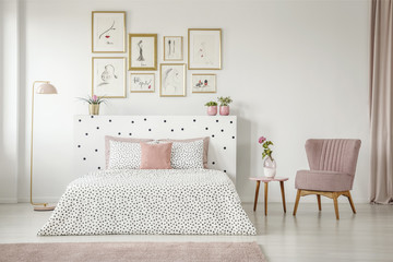 Feminine bedroom interior with white walls, polka dot bedding, pink elements and fashion drawings gallery in golden frames