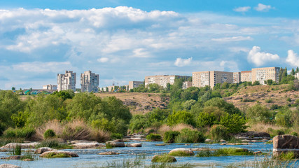 Yuzhnoukrainsk on the rocky bank of the river. Summer landscape with river flow and with stones and green vegetation.