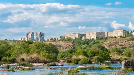 Fototapeta premium Yuzhnoukrainsk on the rocky bank of the river. Summer landscape with river flow and with stones and green vegetation.