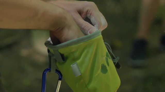 Hand enters chalk bag outside in forest before climbing