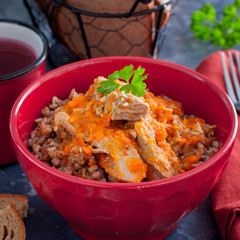 Buckwheat porridge with meat and carrots in a red bowl, square