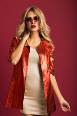 Fototapeta premium Beautiful blonde in a red jacket in the studio on a red background