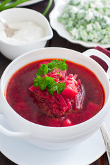 Vegetarian borsch with fresh herbs in a white serving plate, selective focus