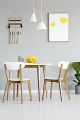 Real photo of a simple, natural dining room interior with lamps and poster with yellow flowers...