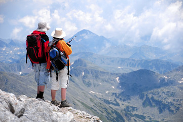 Male and female hikers shoot from the back standing looking at mountain view at Vihren summit,...