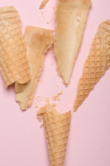 Crushed empty ice cream waffle cone on pink pastel background closeup