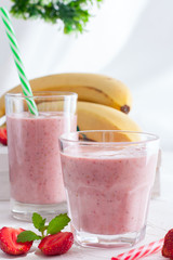 Smoothies of strawberries and bananas in glass glasses on a white table, selective focus