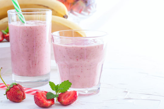 Smoothies of fresh strawberries and bananas in glass glasses on a white table, copy space