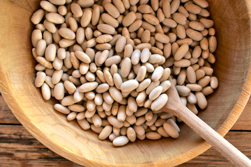 White beans dry, uncooked beans in a wooden bowl, closeup.
