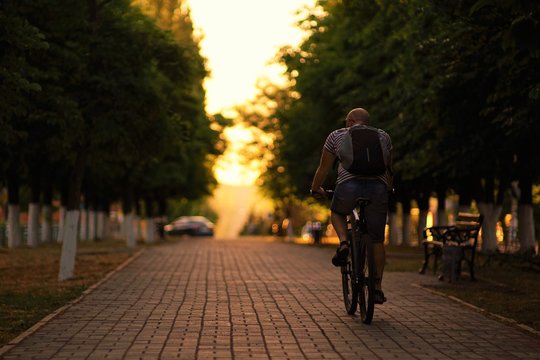Man leisurely rides a bicycle through the alley at sunset