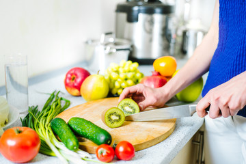 Woman cuts kiwi by the knife on the wooden board at the kitchen