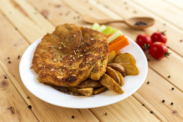 A large piece of fried meat in breadcrumbs. French fries and vegetables