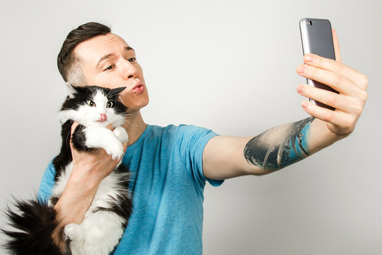 Young hipster does selfie with cat on light gray background.