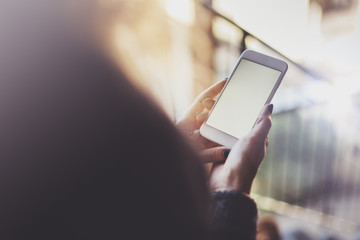 Woman holding hands smartphone and texting message.Female hands using mobile phone.Closeup on blurred background.Flares, bokeh effects. Mock-up.