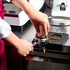 Unidentified barista girl pressing ground coffee with temper int