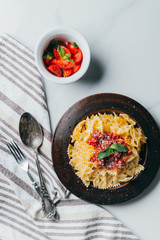 elevated view of plate with pasta, kitchen towel, fork, spoon and bowl with cherry tomatoes on marble table