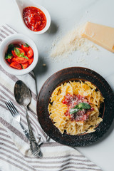 top view of plate with pasta, grated parmesan, bowls with sauce and cherry tomatoes on marble table