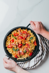 cropped image of man holding pan with pasta covered by grated parmesan with cherry tomatoes, jamon, mint leaves over marble table
