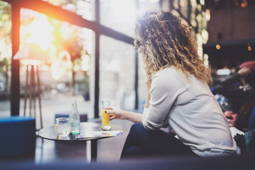 Charming beautiful young woman reading email message on mobile phone during rest time in coffee shop. Bokeh and flares effect on blurred background.