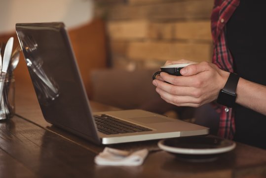 Mid section of man using laptop while having coffee