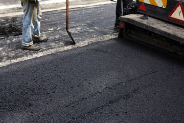 Worker using asphalt paver tool during road construction.
