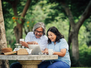 Senior couple looking laptop and have breakfast in the garden together.