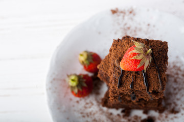 Stack of brownies decorated with strawberries on white plate on white background. Copy space.