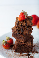 Stack of brownies decorated with strawberries on white plate on white background. Copy space.