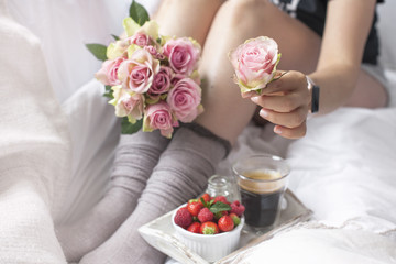 Obraz na płótnie Canvas A bouquet of pink roses in the hands of the girl on the bed, Berries of strawberries and a fragrant morning coffee. Romance. Vintage photo. Copy space.