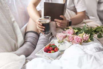 Obraz na płótnie Canvas A bouquet of pink roses, in the hands of a girl's book, Berries of strawberries and fragrant coffee Espresso in the morning. Romantic breakfast in bed. Vintage photo. Copy space.