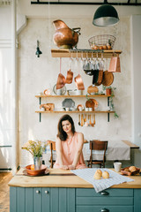 Young beautiful housewife in dress having breakfast on kitchen. Lovely woman posing and dreaming in...