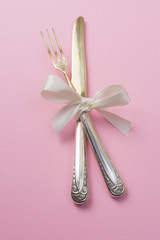 Silver fork and knife with white ribbon on pink background