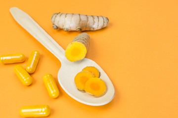 Yellow curcuma root with wooden spoon and pills on orange background