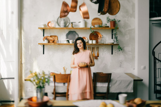 Young Beautiful Housewife In Dress Having Breakfast On Kitchen. Lovely Woman Posing And Dreaming In Country French Style Decorated Interior Zone. Rustic Dining Room With Fresh Food And Tableware.