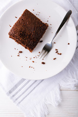 Brownie slice on a white plate on white napkin on white wooden background. Copy space. Flat lay. Overhead