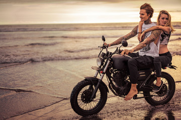 Fototapeta na wymiar passionate couple riding motorcycle on ocean beach during sunrise