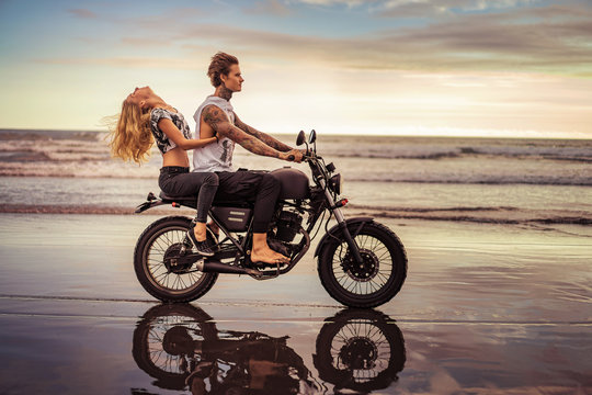 side view of young couple riding motorcycle on ocean beach