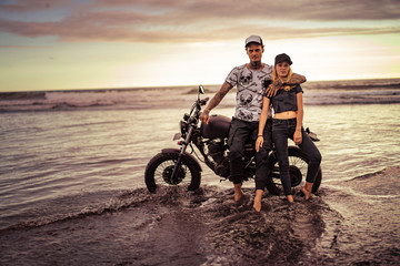 Obraz premium stylish couple standing and cuddling near motorcycle on ocean beach