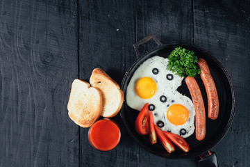scrambled egg with sausages in the pan and tomatoe juice on black background. Copy space