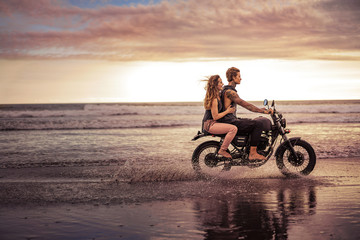 Obraz na płótnie Canvas side view of couple riding motorcycle on ocean beach