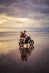 Obraz premium boyfriend and girlfriend sitting on motorcycle at beach during sunrise and cloudy weather