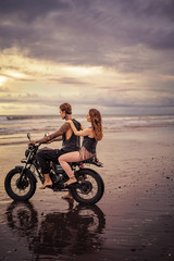 Fototapeta na wymiar side view of couple sitting on motorcycle at beach during sunrise