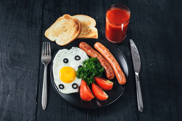 scrambled egg with sausages in the pan and tomatoe juice on black background. Copy space