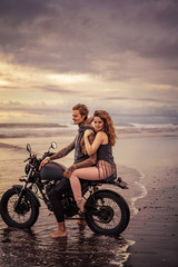 Obraz na płótnie Canvas attractive girlfriend and boyfriend sitting on motorcycle at beach during sunrise