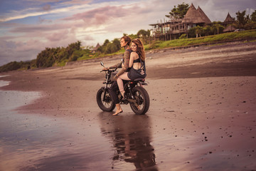Naklejka na ściany i meble boyfriend and girlfriend sitting on motorcycle at beach during sunrise
