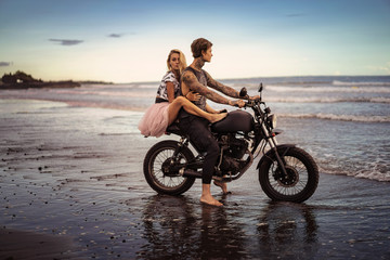 Fototapeta na wymiar side view of couple hugging on motorcycle on ocean beach