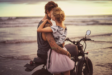 passionate couple hugging on motorcycle on ocean beach during beautiful sunrise